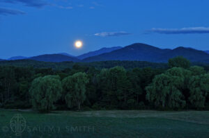 A full moon hangs low over a green and peaceful valley