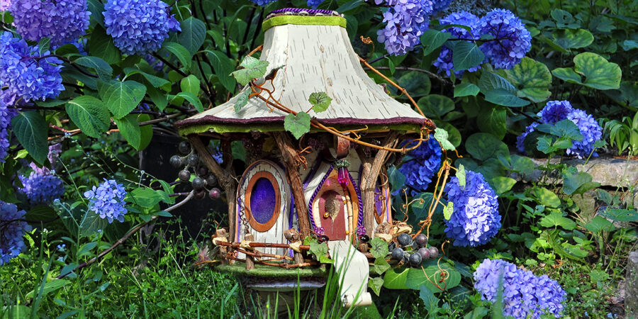 A magical Fairy House with a white roof nestled in deep blue Hydrangea blossoms. Sculpture and photograph by Sally J Smith.