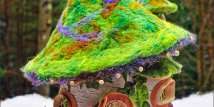 A Birch bark fairy house with bright green and purple felted wool conical roof